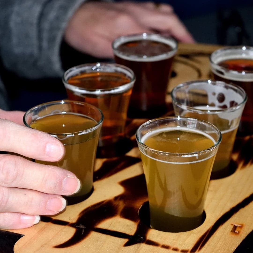 six small glasses of beer on a board