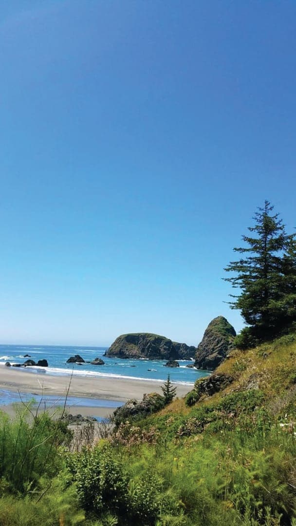 Coastal view featuring sandy beach, rocky outcrops, a calm sea, and a blue sky with a few scattered clouds.