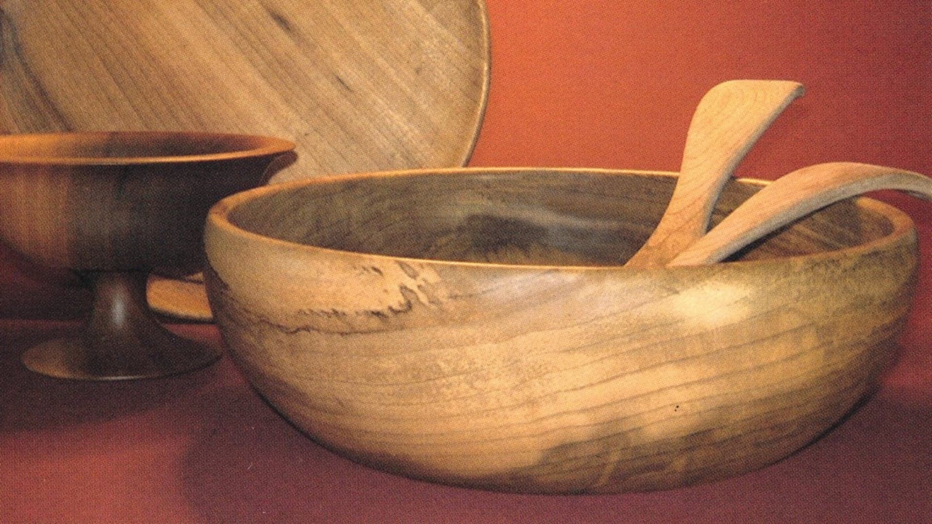 Two wooden bowls and serving utensils against a red background.