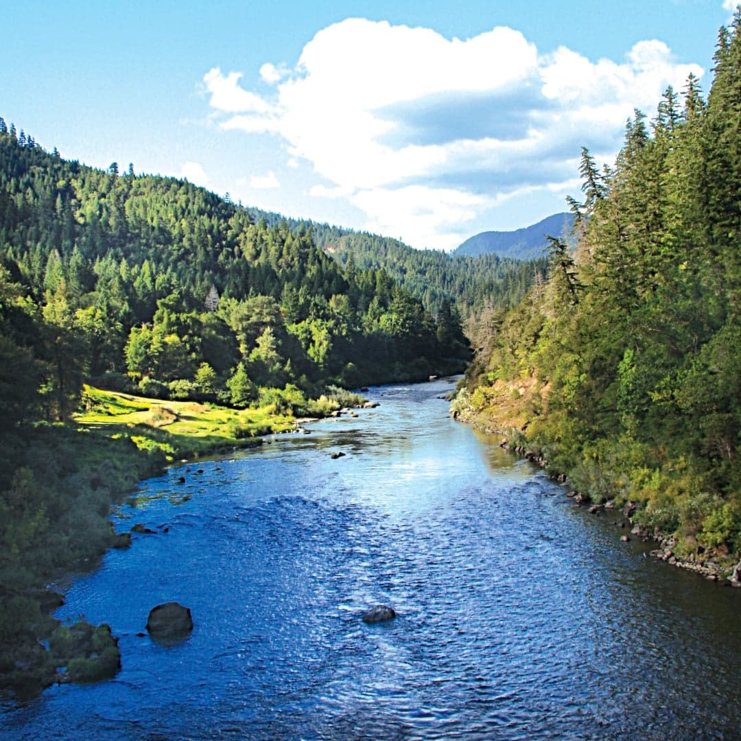 A serene river winding through lush green hills under a partly cloudy sky.