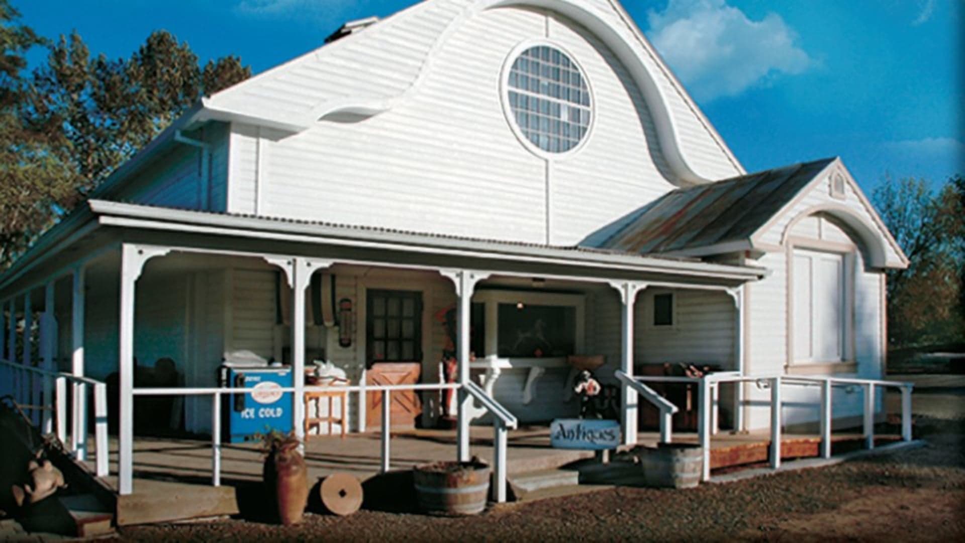 Quaint white building with a porch, featuring a sign that says "Antiques" and blue ice chest at the entrance.