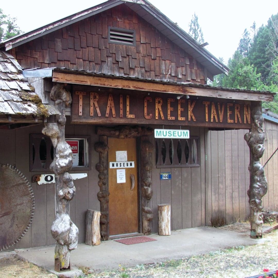 Exterior of Trail Creek Tavern, featuring rustic wooden construction and signs for "Open" and "Museum."