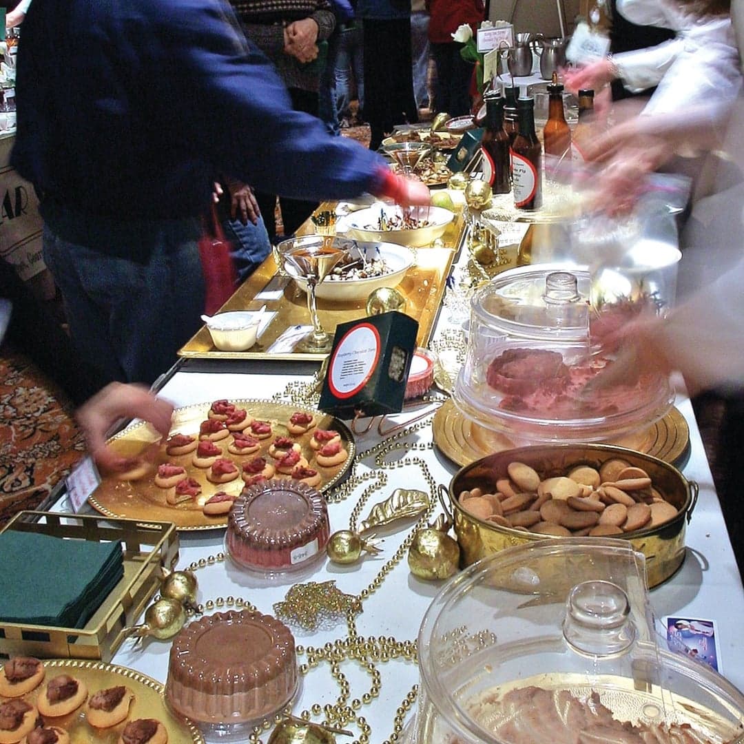 A festive dessert table with various sweets, including cookies and chocolates, and people serving themselves.