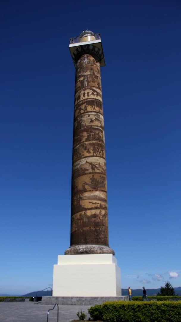 Tall, decorated column under a clear blue sky, with two people walking nearby.