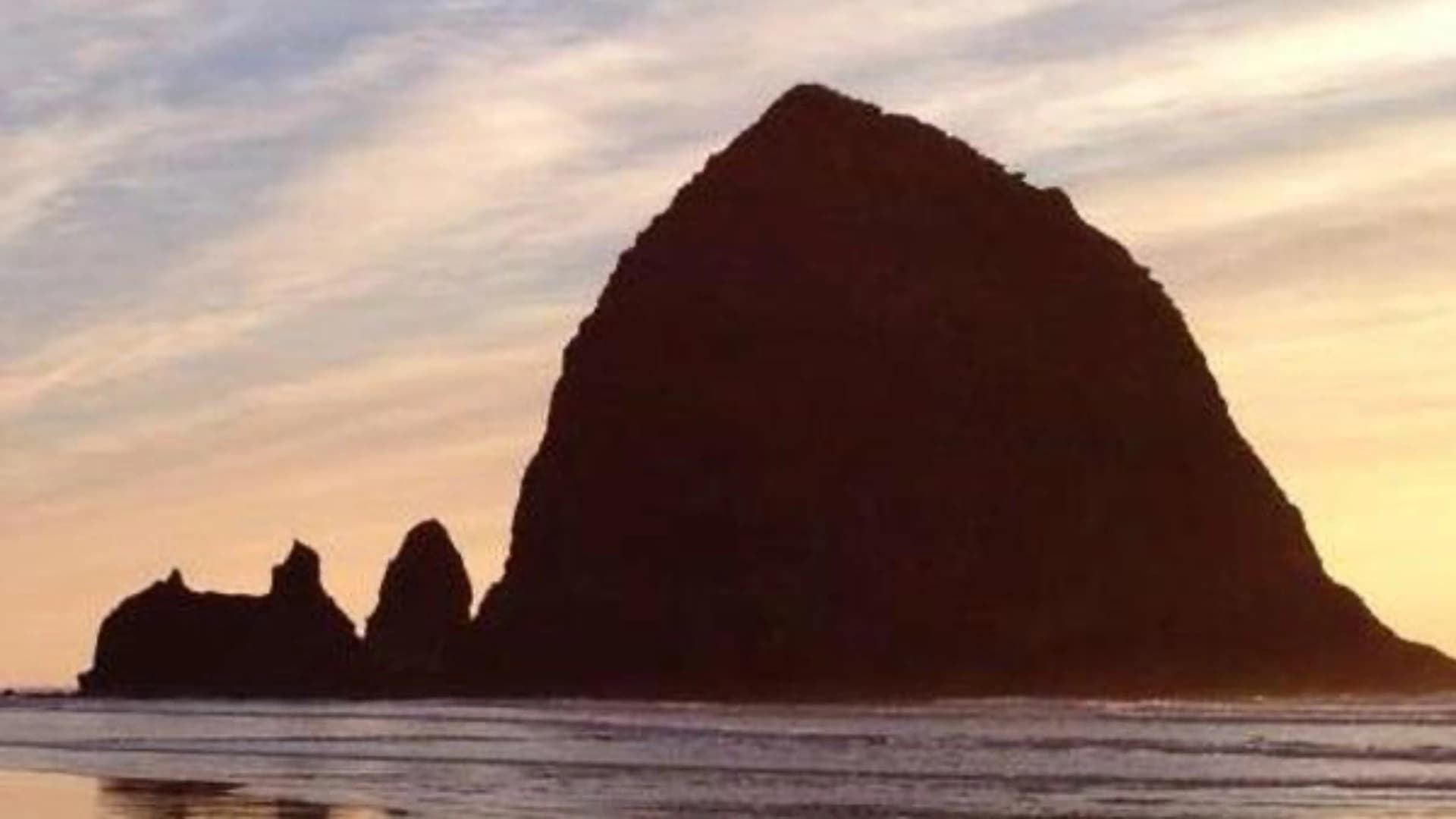 Silhouette of a large rock formation against a colorful sunset sky over the ocean.