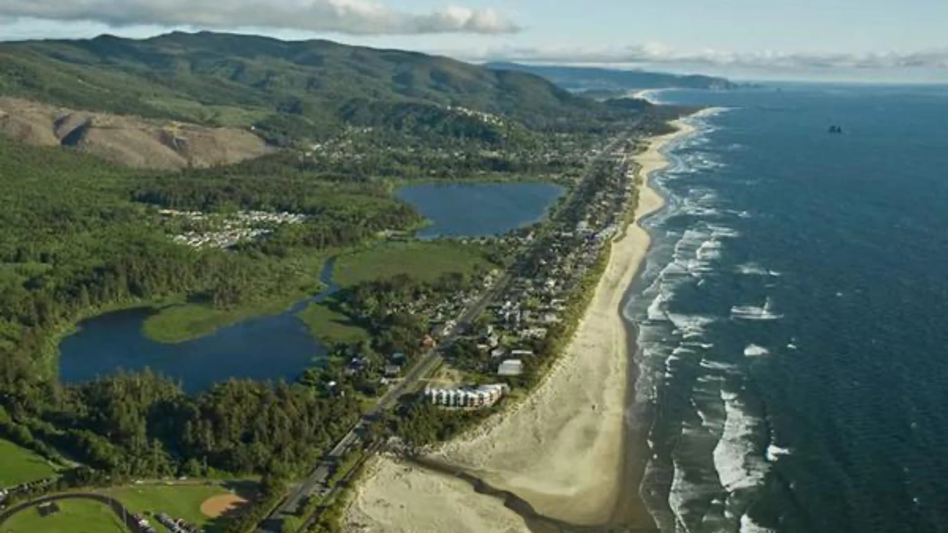 Aerial view of a coastal town with sandy beaches, rolling hills, and calm lakes along the shore.