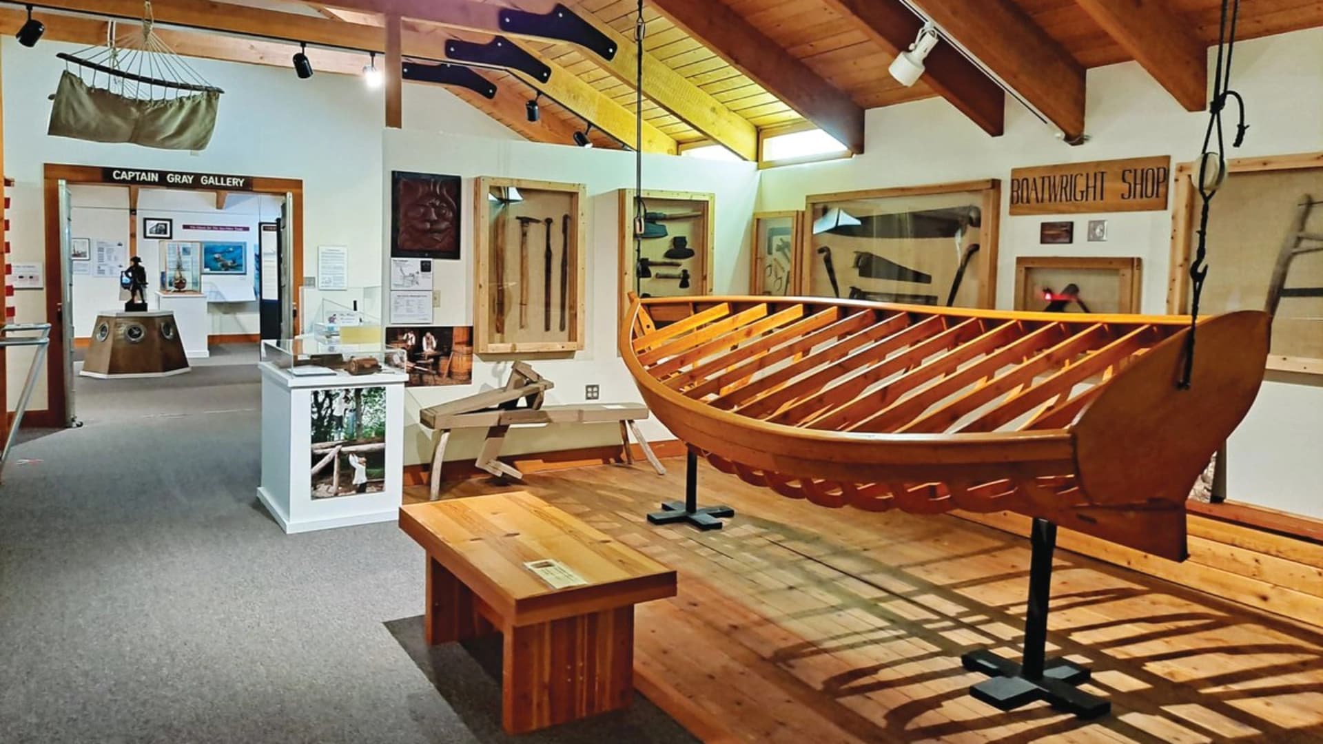 Interior of a museum with a wooden boat exhibit, a bench, and various artifacts on display in glass cases.