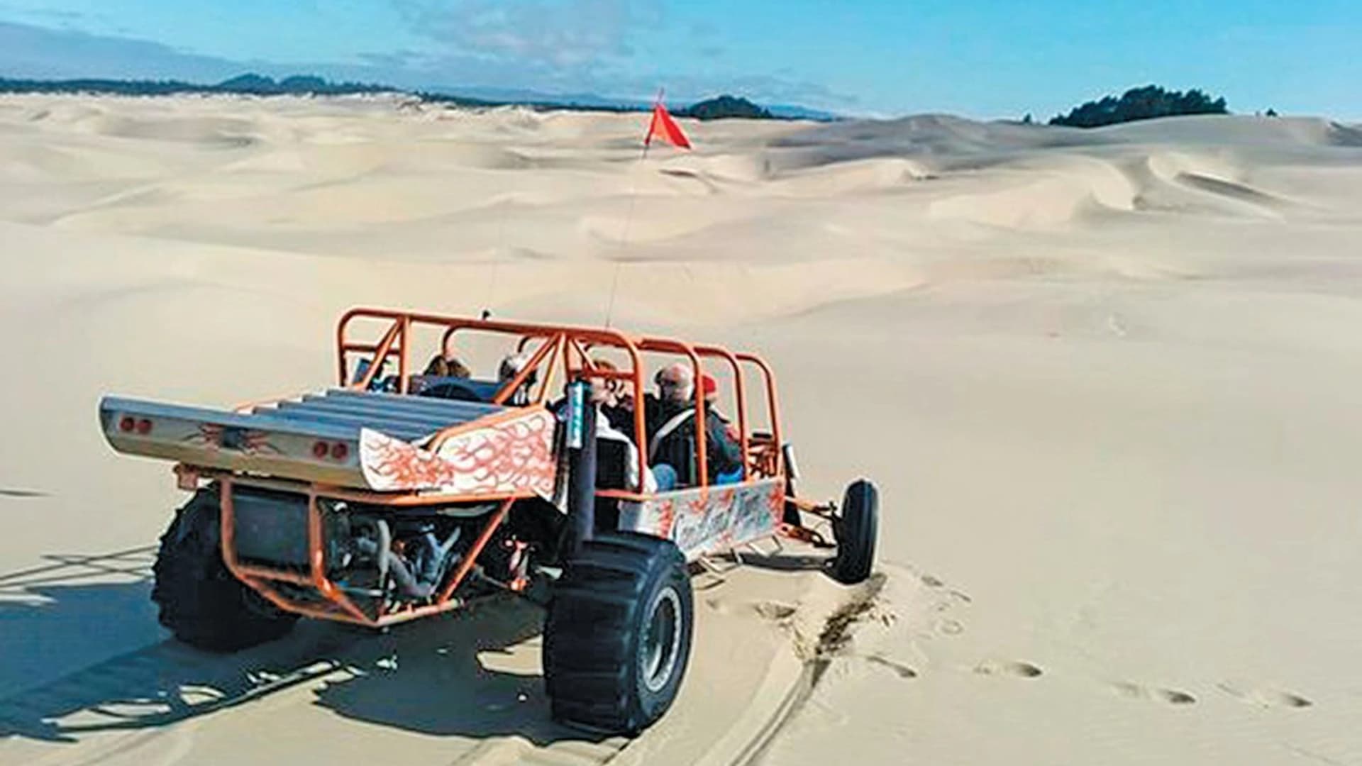 A dune buggy with passengers navigating sandy dunes under a clear blue sky.