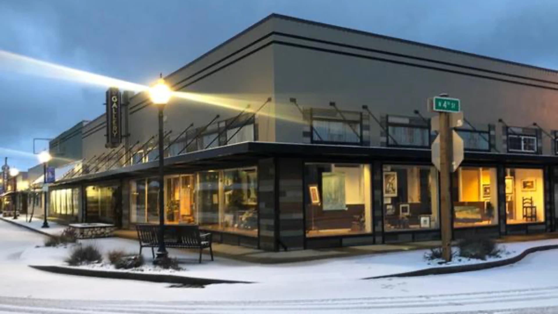 Corner building with gallery windows, snow-covered street, and street sign for 4th Street, under a cloudy sky.