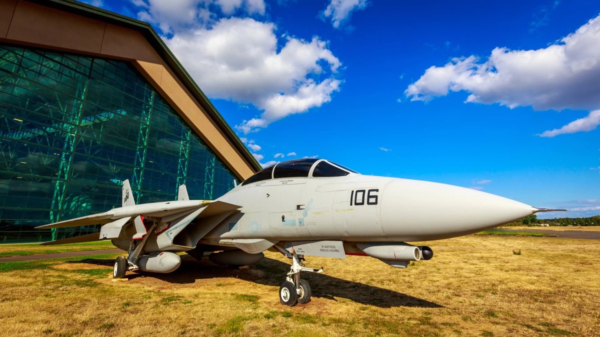 A military fighter jet displayed outside a hangar, with blue skies and clouds in the background.