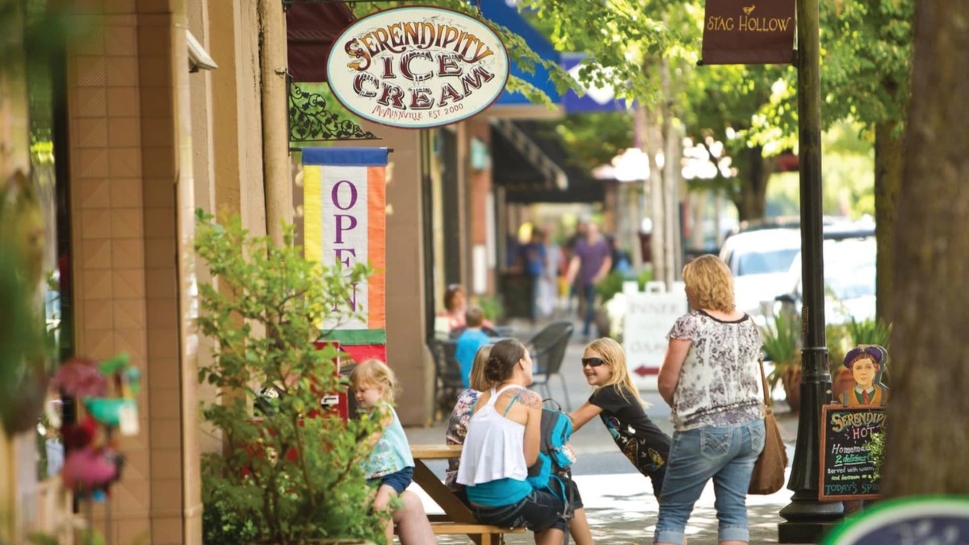 Outdoor scene featuring "Serendipity Ice Cream" shop sign with people enjoying ice cream at tables on a sunny day.