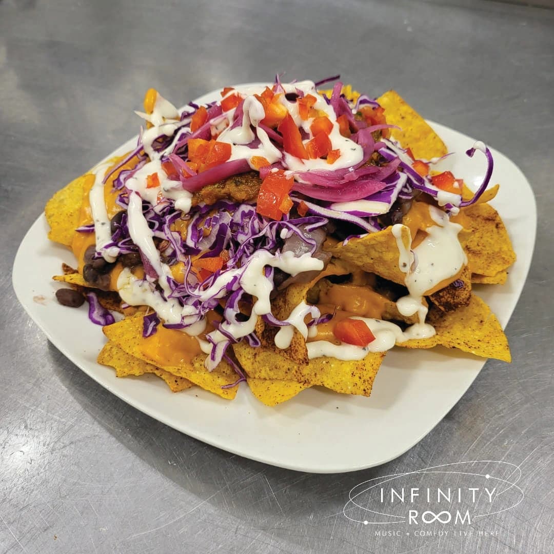 A plate of nachos topped with cheese, black beans, red cabbage, tomatoes, and drizzled with sauce.