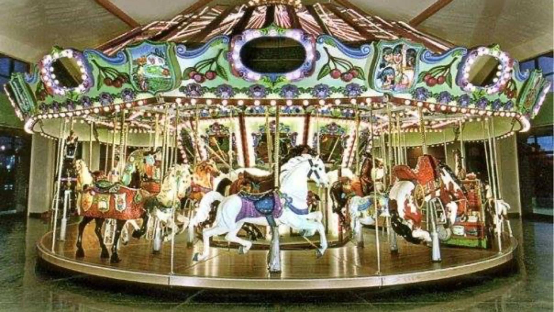 Colorful carousel with ornate horses and lights, situated indoors under a decorative canopy.