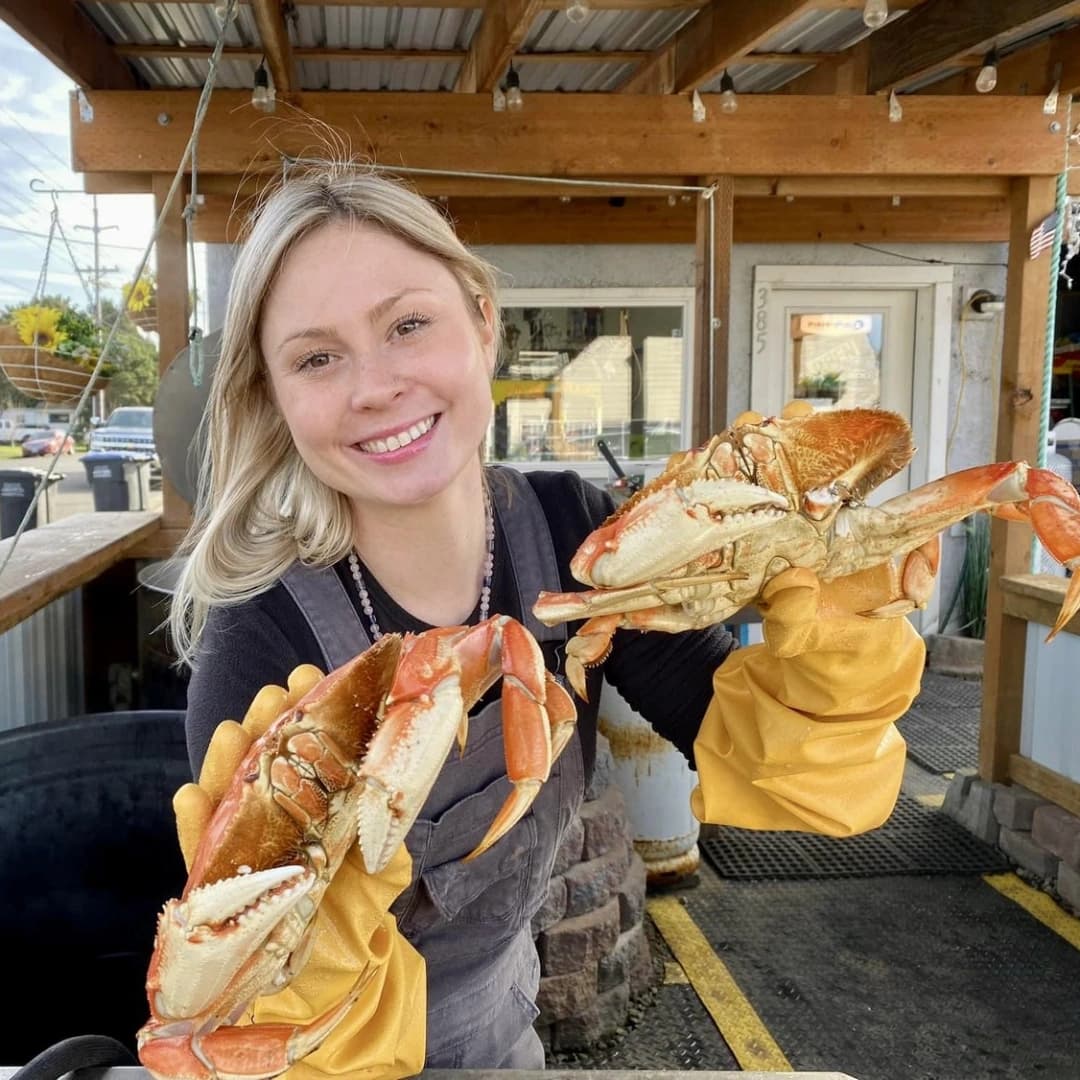 Smiling woman wearing yellow gloves holds two crabs in a seafood market setting.