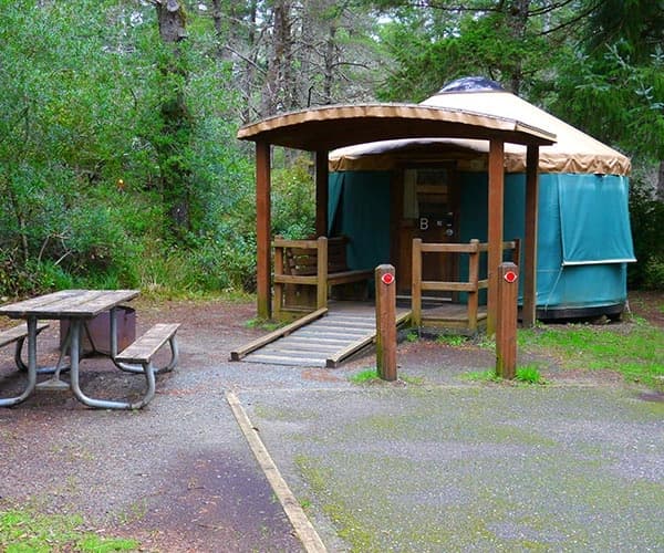 Campsite shelter with open porch and steps in a wooded area; no prominent readable text.